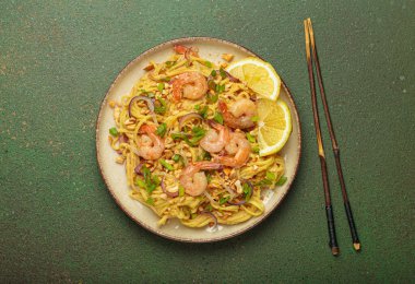 Karides, fıstık, yeşil soğan, limon dilimleri ile süslenmiş Tayland erişteleri ve kırsal yeşil arka planda servis edilen çubuklarla Tayland mutfağı.