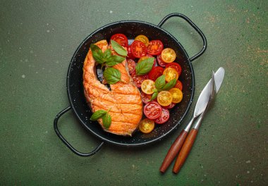 Siyah tavada ızgara somon bifteği, yanında canlı kiraz domatesleri ve taze fesleğen yaprakları, sağlıklı beslenme ya da diyet konsepti.