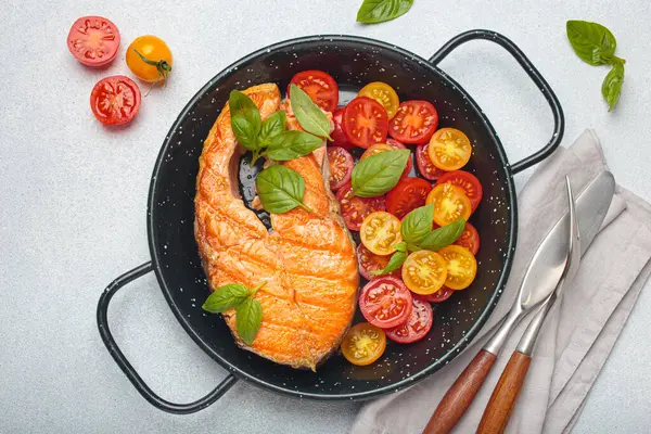 Siyah tavada ızgara somon bifteği, yanında canlı kiraz domatesleri ve taze fesleğen yaprakları, sağlıklı beslenme ya da diyet konsepti.