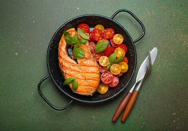 Siyah tavada ızgara somon bifteği, yanında canlı kiraz domatesleri ve taze fesleğen yaprakları, sağlıklı beslenme ya da diyet konsepti.