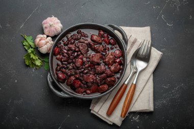 Feijoada, dökme demir bir tencerede geleneksel Brezilya güveci, yanında taze sarımsak ve maydanoz, keten peçetede çatal ve kaşıkla servis edilmeye hazır.