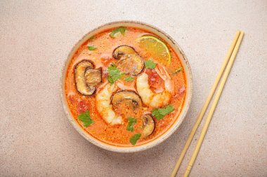 Karides, mantar, limon ve kişniş karışımlı lezzetli Tom çorbası açık bej arka planda yemek çubuklarıyla servis edilir Tayland 'ın aromatik ve geleneksel bir yemeğidir.