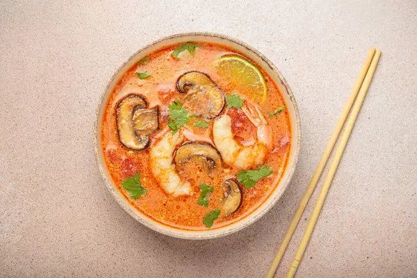 Karides, mantar, limon ve kişniş karışımlı lezzetli Tom çorbası açık bej arka planda yemek çubuklarıyla servis edilir Tayland 'ın aromatik ve geleneksel bir yemeğidir.