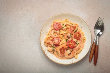 Karides ve kiraz domatesli kremalı deniz ürünleri makarna, taze maydanozla süslenmiş, açık bej arka planda servis edilmiş, çatal bıçak üst görüşlü, kopyalama alanı