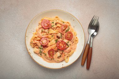 Taze maydanozla süslenmiş karides ve kiraz domatesli kaymak soslu deniz ürünleri linguine makarna, açık bej arka planda servis edilir.