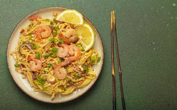 Karides, fıstık, yeşil soğan, limon dilimleri ile süslenmiş Tayland erişteleri ve kırsal yeşil arka planda servis edilen çubuklarla Tayland mutfağı, fotokopi alanı.