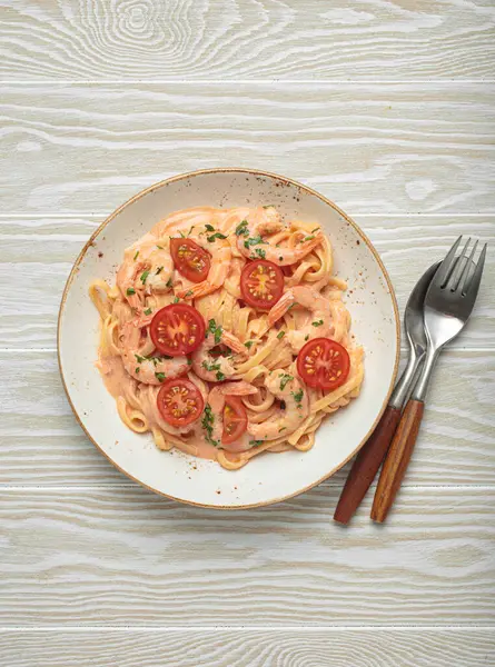 Taze maydanozla süslenmiş karides ve kiraz domatesli kaymak soslu deniz ürünleri linguine makarna beyaz ahşap arka planda servis edilir.