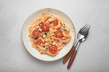 Taze maydanozla süslenmiş karides ve kiraz domatesli kaymak soslu deniz ürünleri linguine makarna açık gri arka planda servis edilir.