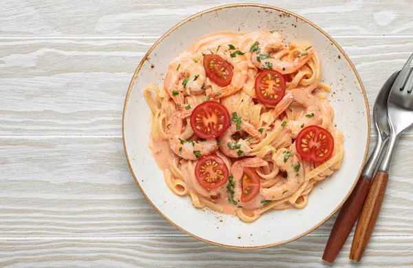 Taze maydanozla süslenmiş karides ve kiraz domatesli kaymak soslu deniz ürünleri linguine makarna, beyaz ahşap arka planda servis ediliyor, üst görünümü var, uzay kopyası var.