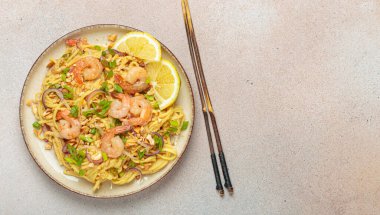 Karides, fıstık, yeşil soğan, limon dilimleri ile süslenmiş Tayland erişteleri bej arka planda çubuklarla servis ediliyor, Tayland mutfağı, fotokopi alanı.