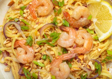 Lezzetli Tayland eriştelerine yakın pişmiş karides, kavrulmuş fıstık, doğranmış yeşil soğan, kırmızı soğan halkaları ve limon dilimi, geleneksel Tayland yemeği.