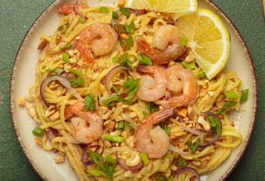 Lezzetli Tayland eriştelerine yakın pişmiş karides, kavrulmuş fıstık, doğranmış yeşil soğan, kırmızı soğan halkaları ve limon dilimi, geleneksel Tayland yemeği.