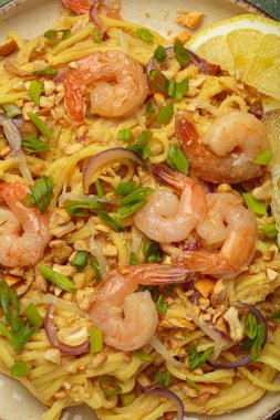 Lezzetli Tayland eriştelerine yakın pişmiş karides, kavrulmuş fıstık, doğranmış yeşil soğan, kırmızı soğan halkaları ve limon dilimi, geleneksel Tayland yemeği.
