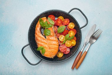 Siyah tavada ızgara somon bifteği, yanında canlı kiraz domatesleri ve taze fesleğen yaprakları, sağlıklı beslenme ya da diyet konsepti.