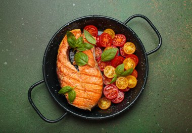 Siyah tavada ızgara somon bifteği, yanında canlı kiraz domatesleri ve taze fesleğen yaprakları, sağlıklı beslenme ya da diyet konsepti.