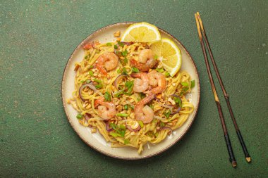 Karides, fıstık, yeşil soğan, limon dilimleri ile süslenmiş Tayland erişteleri ve kırsal yeşil arka planda servis edilen çubuklarla Tayland mutfağı.