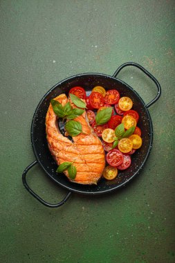 Siyah tavada ızgara somon bifteği, yanında canlı kiraz domatesleri ve taze fesleğen yaprakları, sağlıklı beslenme ya da diyet konsepti.