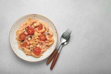 Karides ve kiraz domatesli kaymak soslu deniz ürünleri linguine makarna, taze maydanozla süslenmiş, açık gri arka planda servis edilen çatal bıçaklı üst manzara, kopyalama alanı.