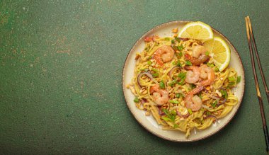 Karides, fıstık, yeşil soğan, limon dilimleri ile süslenmiş Tayland erişteleri ve kırsal yeşil arka planda servis edilen çubuklarla Tayland mutfağı, fotokopi alanı.