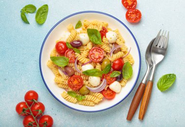 İtalyan fusilli makarna salatası, taze vişneli domates, mozzarella, zeytin, kırmızı soğan ve fesleğen yaprağı, İtalyan mutfak geleneği kavramı.