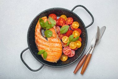 Siyah tavada ızgara somon bifteği, yanında canlı kiraz domatesleri ve taze fesleğen yaprakları, sağlıklı beslenme ya da diyet konsepti.