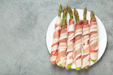 Pastırma şeritlerine sarılmış lezzetli kuşkonmaz, renkli biberlerle tatlandırılmış, beyaz bir tabakta sunulmuş, pişirilmeye hazır, uzay kopyası