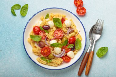 İtalyan fusilli makarna salatası, taze vişneli domates, mozzarella, zeytin, kırmızı soğan ve fesleğen yaprağı, İtalyan mutfak geleneği kavramı.