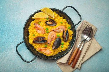 Pirinç, karides, midye, bezelye ve limon dilimli deniz ürünleri paella koyu kırsal bir arka planda, zeytin ve çatal bıçaklı siyah geleneksel bir tavada servis edilir, Akdeniz yemeği.