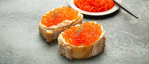 Kırmızı somon havyarlı küçük metal tabak ve iki havyar tostu gri beton arka planda kanepe, şenlikli lüks lezzet ve aperatif..