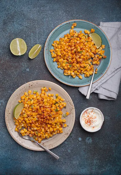 İki tabak esquite, popüler bir Meksika sokak yemeği, limon dilimleri ve acı biberli ekşi krema ile servis edilir.