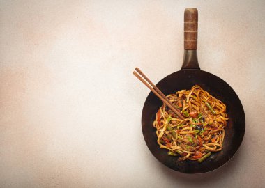 Kızarmış tavuk ve sebzeli erişteli tava, tepesinde tahta çubuklar, açık bej arka planda üst manzara, kopyalama alanı