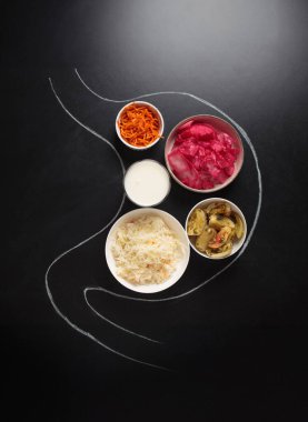 Lahana turşusu, turşu turşusu, kimçi ve yoğurt gibi mayalanmış gıdalar, sağlıklı bir bağırsak mikrobiyomunun korunmasında yararlı rollerini sembolize eden bir tebeşirle midenin ana hatları içinde düzenlenir.