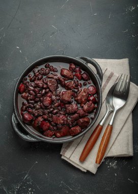 Feijoada, dökme demir bir tencerede geleneksel Brezilya güveci, keten peçetede çatal ve kaşıkla servis edilmeye hazır.