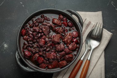 Feijoada, dökme demir bir tencerede geleneksel Brezilya güveci, keten peçetede çatal ve kaşıkla servis edilmeye hazır.