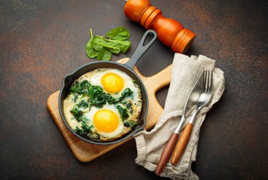 Tahta bir tahtanın üzerinde ıspanaklı iki sahanda yumurta, sağlıklı bir kahvaltı.