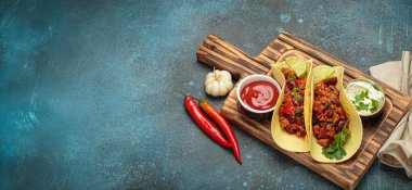 Biberli takolar, fasulyeler, maydanoz, limon, ekşi krema ve domates sosu ahşap bir tahtanın üzerinde, Meksika mutfağında canlı bir deneyim.