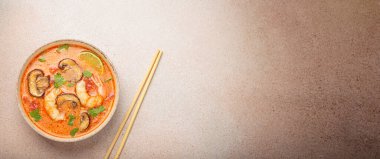 Karides, mantar, limon ve kişniş karışımlı lezzetli Tom çorbası açık bej arka planda yemek çubuklarıyla servis edilir Tayland 'ın aromatik ve geleneksel bir yemeğidir.