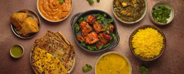 Kahverengi masadaki çeşitli Hint yemeklerinin genel görünümü, köri, tandır tavuğu, tavuk tikka masala, dal, Palak paneer, paratha, pirinç, samosa, Hindistan 'ın zengin aşçılık mirası