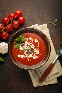 Taze domates çorbası krema, tohum ve otlarla dolu bir kasede servis edilir. Yanında da kaşık ve peçeteyle birlikte kiraz domatesleri, sarımsak ve maydanoz bulunur.