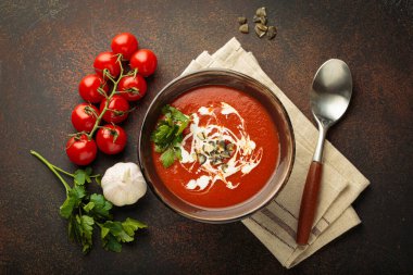 Taze domates çorbası krema, tohum ve otlarla dolu bir kasede servis edilir. Yanında da kaşık ve peçeteyle birlikte kiraz domatesleri, sarımsak ve maydanoz bulunur.