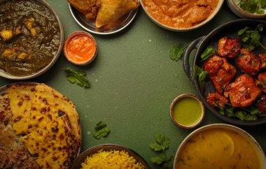 Yeşil bir masadaki çeşitli Hint yemeklerinin genel görünümü, köri, tandır tavuğu, tavuk tikka masala, dal, Palak paneer, paratha, pilav, samosa gibi. Hindistan mutfağı, kopyalama alanı