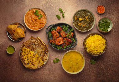 Kahverengi masadaki çeşitli Hint yemeklerinin genel görünümü, köri, tandır tavuğu, tavuk tikka masala, dal, Palak paneer, paratha, pirinç, samosa, Hindistan 'ın zengin aşçılık mirası