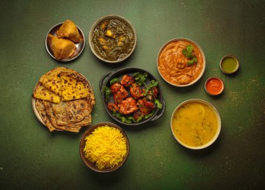 Yeşil masadaki çeşitli Hint yemeklerinin genel görünümü, köri, tandır tavuğu, tavuk tikka masala, dal, Palak paneer, paratha, pirinç, samosa, Hindistan 'ın zengin mutfak mirası