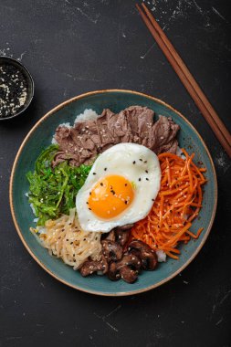 Bibimbap, haşlanmış pirinçli otantik Kore yemeği, kızarmış yumurta, sığır eti, renkli sebzeler, Kore 'nin geleneksel siyah arka plan manzarası.