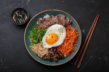 Bibimbap, haşlanmış pirinçli otantik Kore yemeği, kızarmış yumurta, sığır eti, renkli sebzeler, Kore 'nin geleneksel siyah arka plan manzarası.