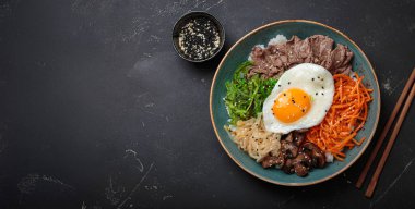 Bibimbap, haşlanmış pirinçli otantik Kore yemeği, kızarmış yumurta, sığır eti, renkli sebzeler, Kore 'nin geleneksel siyah arka plan manzarası.