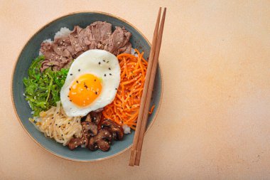 Bibimbap, haşlanmış pirinçli otantik Kore yemeği, kızarmış yumurta, sığır eti, renkli sebzeler, Kore 'nin geleneksel bej arka plan manzarası.