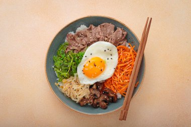 Bibimbap, haşlanmış pirinçli otantik Kore yemeği, kızarmış yumurta, sığır eti, renkli sebzeler, Kore 'nin geleneksel bej arka plan manzarası.