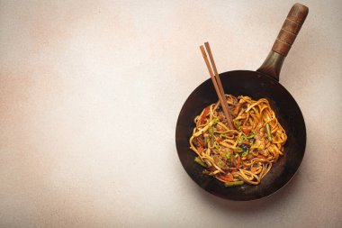 Kızarmış tavuk ve sebzeli erişteli tava, tepesinde tahta çubuklar, açık bej arka planda üst manzara, kopyalama alanı