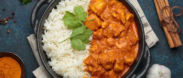 Hintli tavuk tikka masala kremalı domates soslu, basmati pilavı, taze kişniş ve baharatla servis ediliyor, geleneksel Hint yemeği.